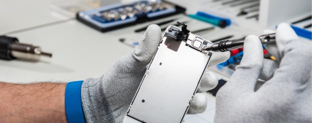 iPhone repair: Close-up of gloved hands holding a phone screen during a repair process.